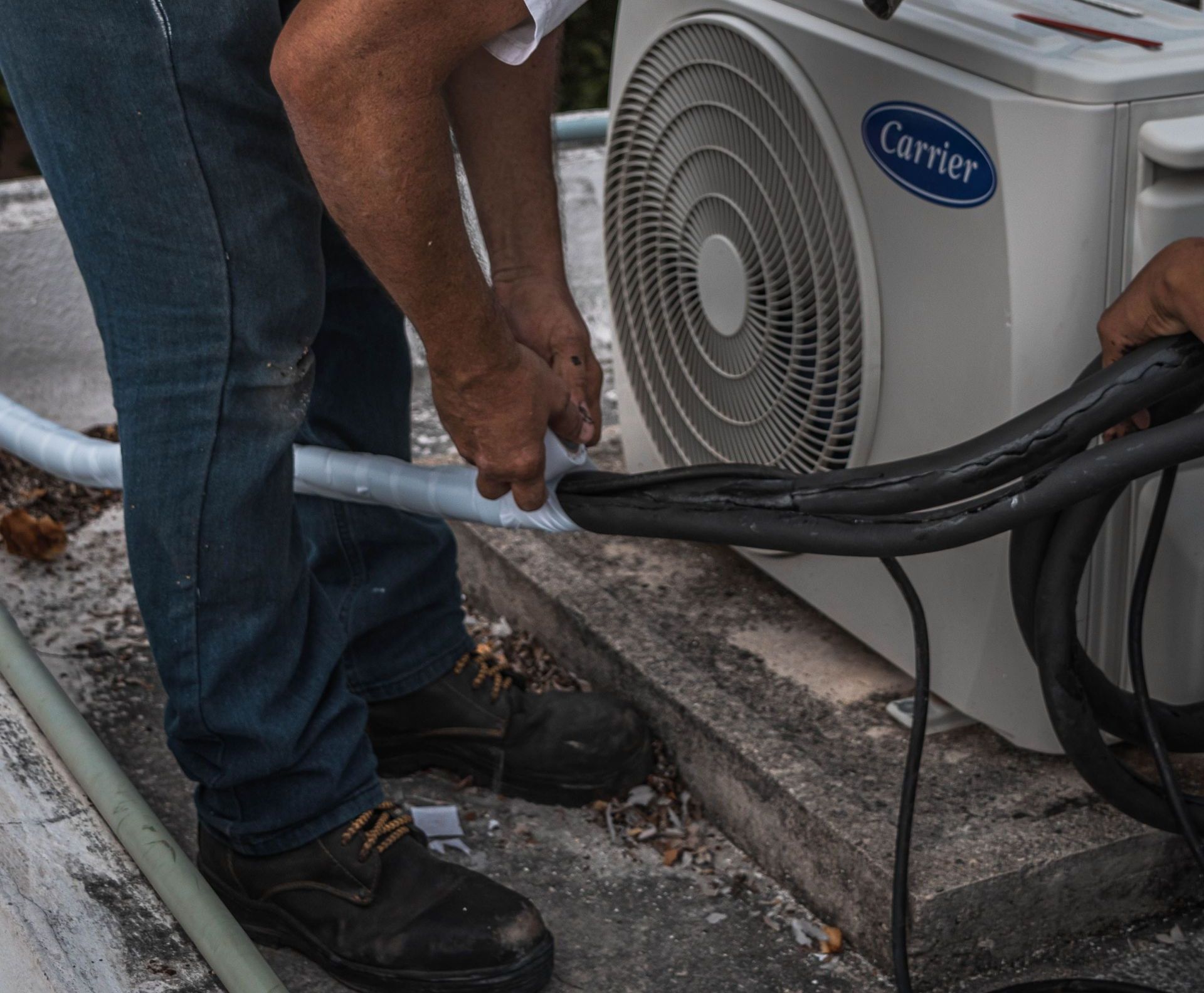 A technician performs maintenance on an outdoor air conditioning unit, focusing on hose connections.